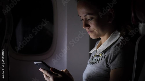Woman with smartphone sitting in airplane near window at night