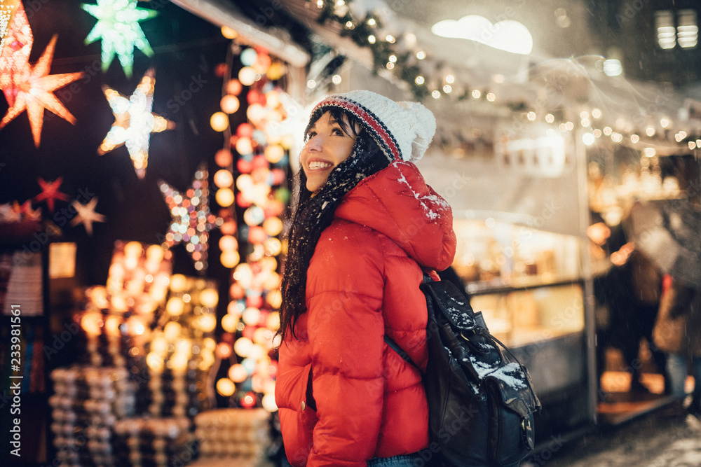 Beautiful happy woman looking for a present on Christmas city fair during snow storm
