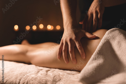A masseur in a dark room does a hip massage with oil for a woman. Spa procedures massage women