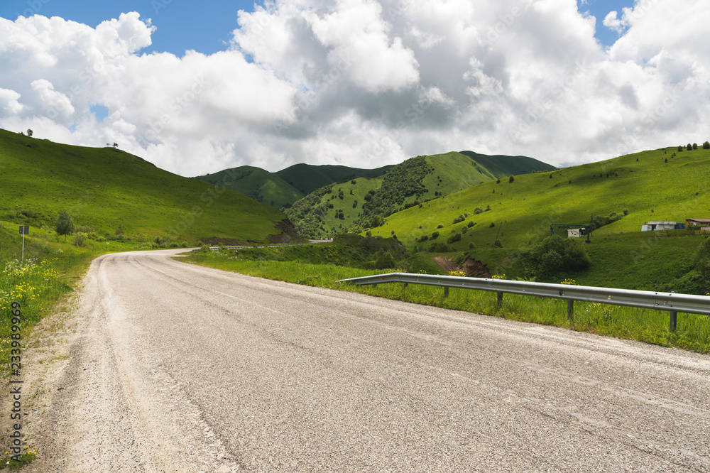 Sunny summer landscape with an asphalt road surrounded by hills and meadows
