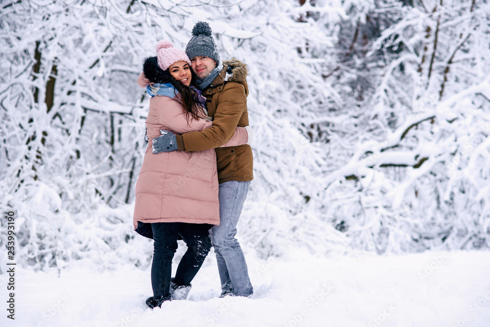 Beautiful pregnant woman dressed in warm clothes walking with her lovely husband in snowy winter park.