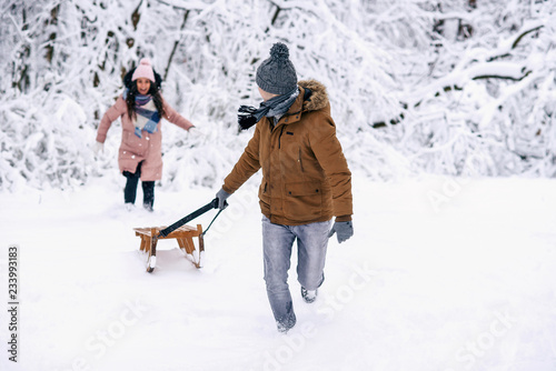 A young man in warm clothes escapes from his wife in a winter park. The young couple have fun in the snowy park.