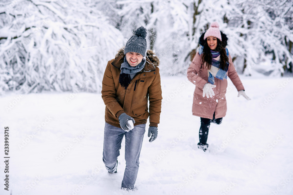 Loving young couple playing with snowballs in a winter park. Family love and care concept.