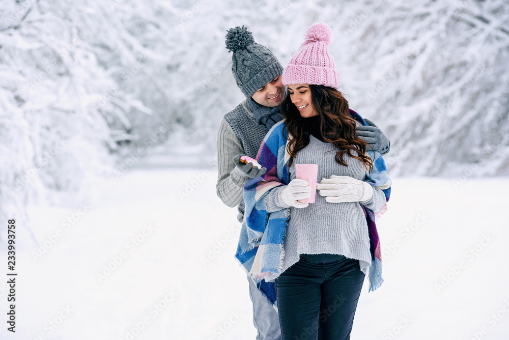 Young man hugs his pregnant wife gently while walking in a snowy park. Family love and care concept. Young man hugs his pregnant wife gently while walking in a snowy park. Family love and care concept.