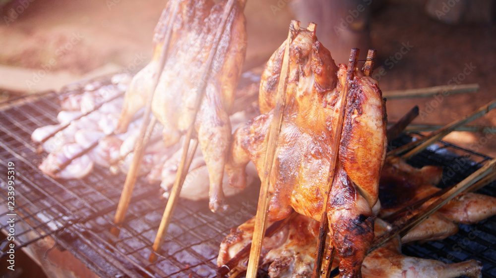 Thai style grilled chicken / Roasting BBQ chicken with garnish in bamboo stick thai style food chicken grilled on the grill in street food Thai style grilled chicken / Roasting BBQ chicken with garnish in bamboo stick thai style food chicken grilled on the grill in street food