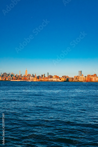 Skyline of midtown Manhattan over Hudson River under blue sky, at sunset, in New York City, USA