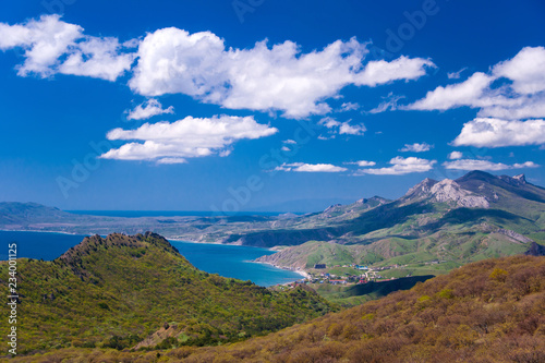 view from the mountains to the seashore with clouds in the blue sky