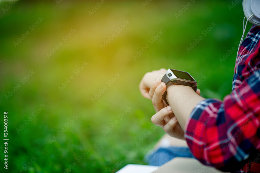 The girl watches the watch in hand, watches the time in a black watch, wears a red shirt and a green background. And there is a copy space. The girl watches the watch in hand, watches the time in a black watch, wears a red shirt and a green background. And there is a copy space.