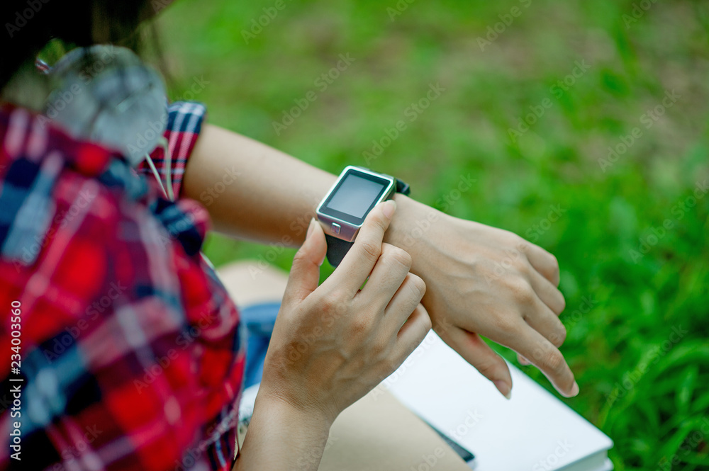 The girl watches the watch in hand, watches the time in a black watch, wears a red shirt and a green background. And there is a copy space.