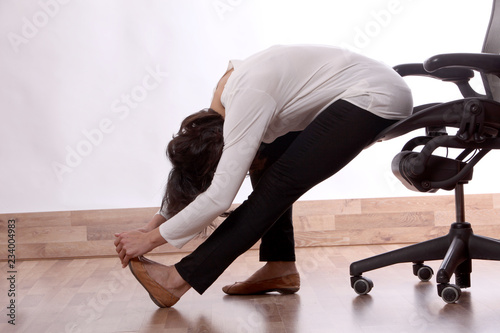 Business woman practices exercises at work place, peaceful woman enjoys stretching on the office chair.