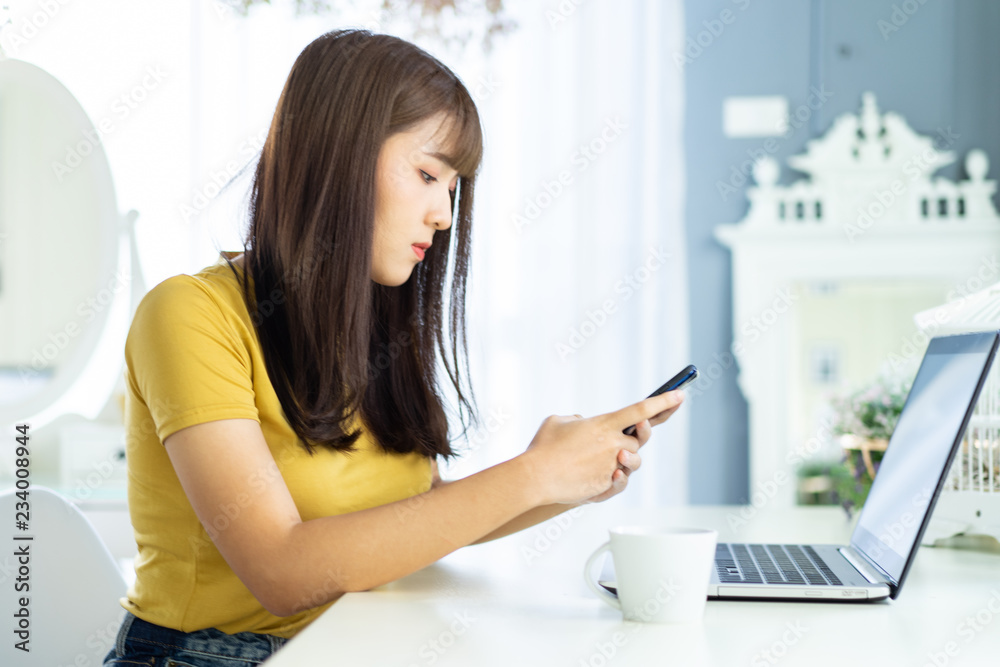 Happy asian beautiful woman working on a laptop sitting on the table in the house.Morning she dress sweater and work at home . Happy asian beautiful woman working on a laptop sitting on the table in the house.Morning she dress sweater and work at home .