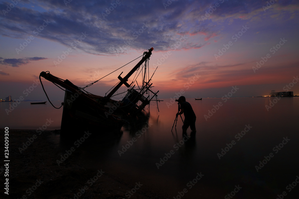 silhouette photographer stand shooting wooden fisherman Shipwrecked with orange sky or twilight sky background