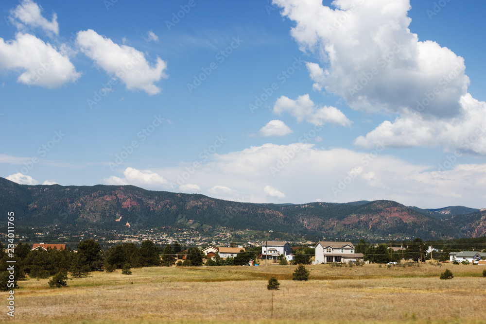 Scenic mountains, clear deep sky with white clouds on a summer sunny day. At the foot of the mountains are located houses of small American cities. Colorado, USA. Scenic mountains, clear deep sky with white clouds on a summer sunny day. At the foot of the mountains are located houses of small American cities. Colorado, USA.
