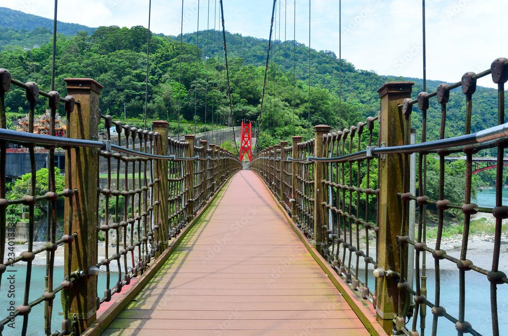 Obraz premium the walkway on red hanging bridge or suspension bridge above the green river in the valley, Wulai, Taiwan