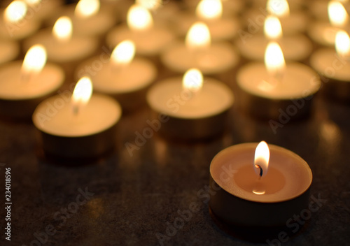 Round tea light candles burning in darkness. Advent or memorial prayer candle flame.
