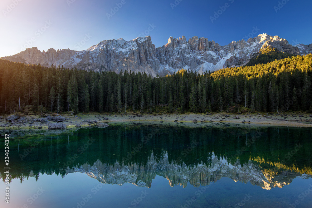 Beautiful sunrise at Carezza lake with light hitting the peaks, Dolomites, Italy