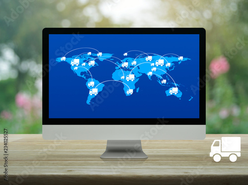 Delivery truck icon with connection line and world map on computer monitor screen on wooden table over blur flower and tree, Business transportation concept, Elements of this image furnished by NASA