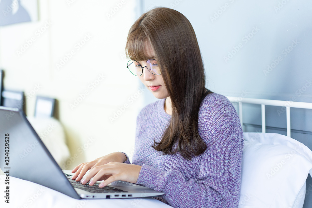 Asian woman working on bed .She dress sweater violet colour.Morning check email internet from notebook. Asian woman working on bed .She dress sweater violet colour.Morning check email internet from notebook.