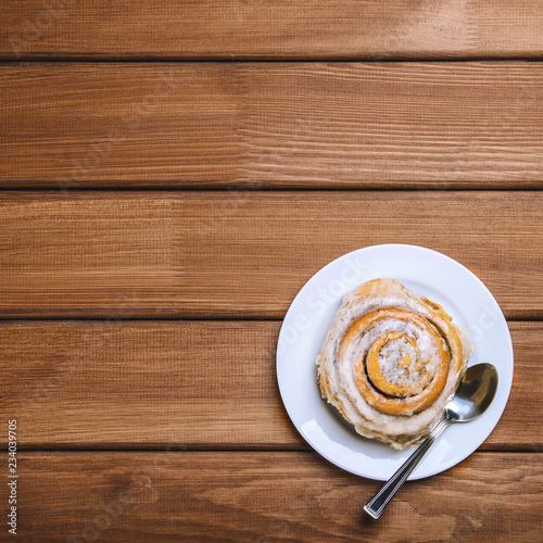 Cinnamon bun on a white plate on a dark wooden background. Top view, copy space, flat lay