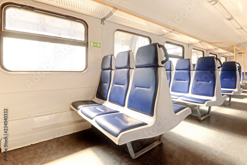 commuter passenger train car interior cabin on sunny day at station with seat sun in window support handle exit sign panorama inside view rail road railway travel transportation lanscape background