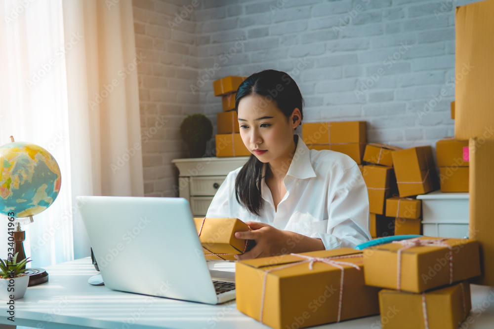 Small business owner, woman checking purchase order in mobile phone and write in the delivery on package box working at home office. online marketing is startup SME entrepreneur and freelance concept. Small business owner, woman checking purchase order in mobile phone and write in the delivery on package box working at home office. online marketing is startup SME entrepreneur and freelance concept.