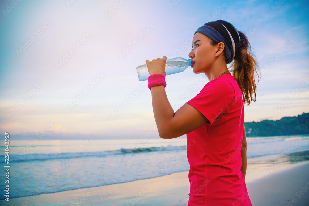 Asian women jogging workout on the beach in the morning. Relax with the sea walk and drinking water from the plastic bottles Asian women jogging workout on the beach in the morning. Relax with the sea walk and drinking water from the plastic bottles