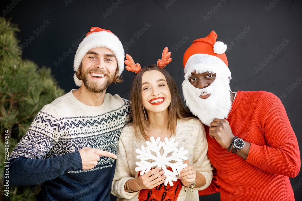Fototapeta premium Young friends dressed in sweaters with New Year hats celebrating winter holidays together indoors