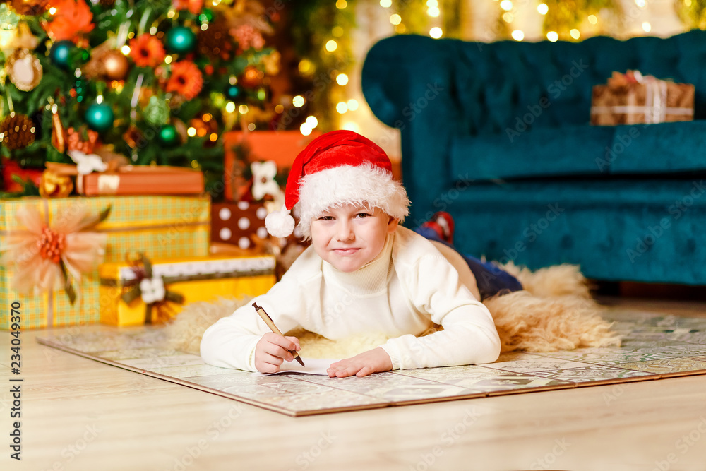 cute smiling boy in Santa's red cap writes a letter to Santa Claus for Christmas cute smiling boy in Santa's red cap writes a letter to Santa Claus for Christmas