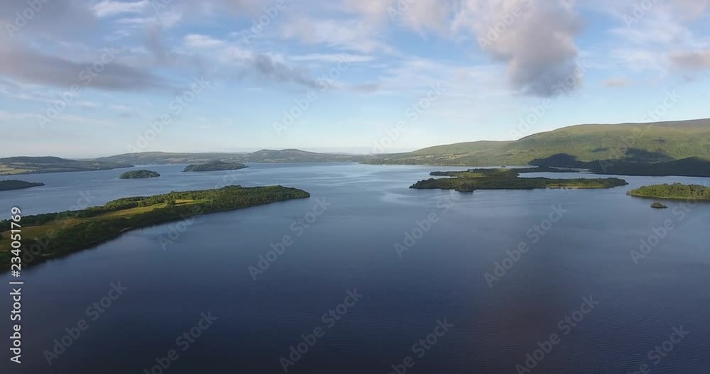 Scottish Loch Featuring a Distant Landscape with Green Hills - Loch Lomond inside The Trossachs National Park Scottish Loch Featuring a Distant Landscape with Green Hills - Loch Lomond inside The Trossachs National Park