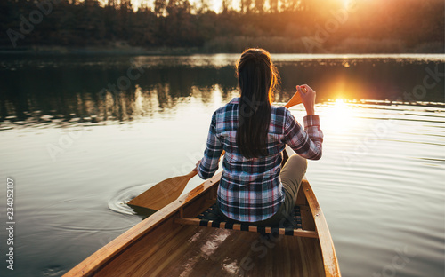 Rear view of hipster girl paddling the canoe on the sunset lake