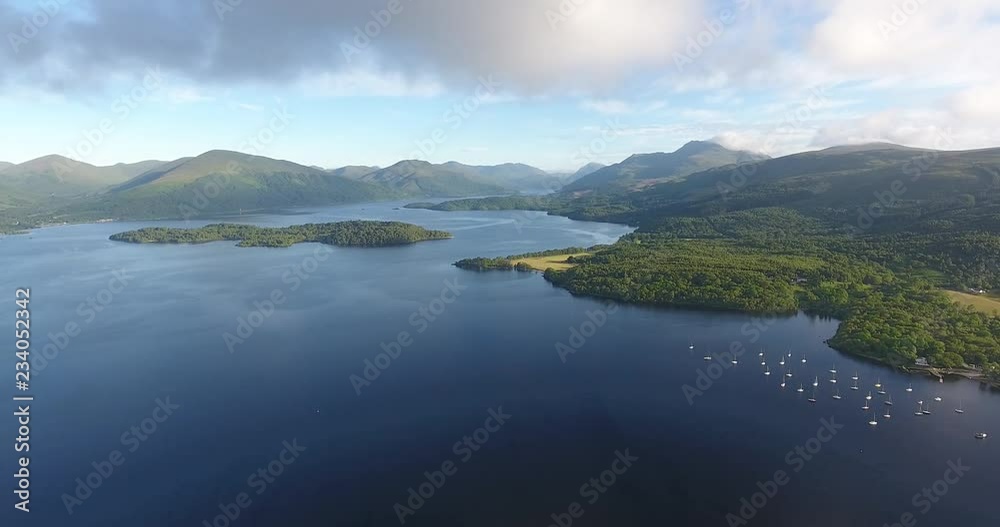 Scottish Loch Featuring a Distant Landscape with Green Hills - Loch Lomond inside The Trossachs National Park Scottish Loch Featuring a Distant Landscape with Green Hills - Loch Lomond inside The Trossachs National Park