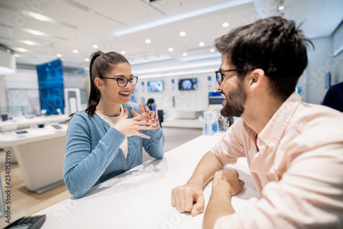 Satisfied female customer on the cashier talking to man that working at tech store.
