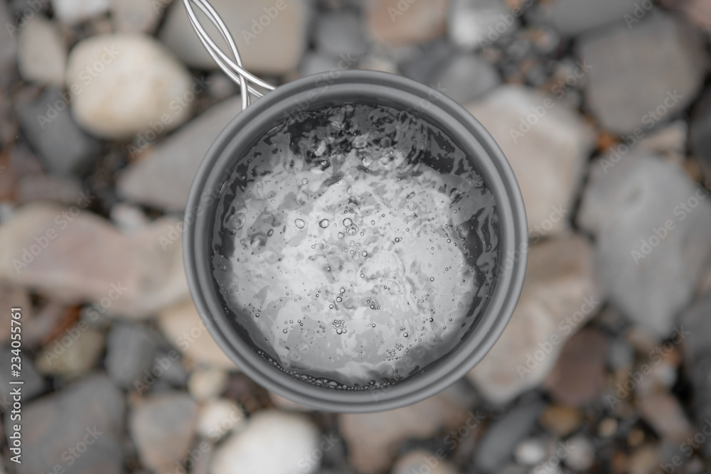 Metal Gray Mug With Boiling Water Close-Up On Background Of River Stones, Top View. Boiling Water In The Campaign. Metal Gray Mug With Boiling Water Close-Up On Background Of River Stones, Top View. Boiling Water In The Campaign.