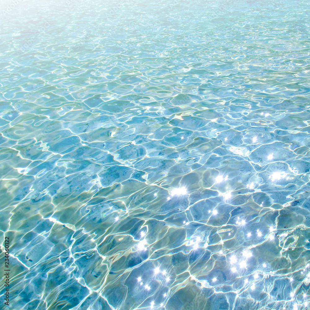 Blue transparent water surface with bright sun glare and sunny shining reflections on bottom. Top view of turquoise ripple texture with sunlight refracting through liquid layer.