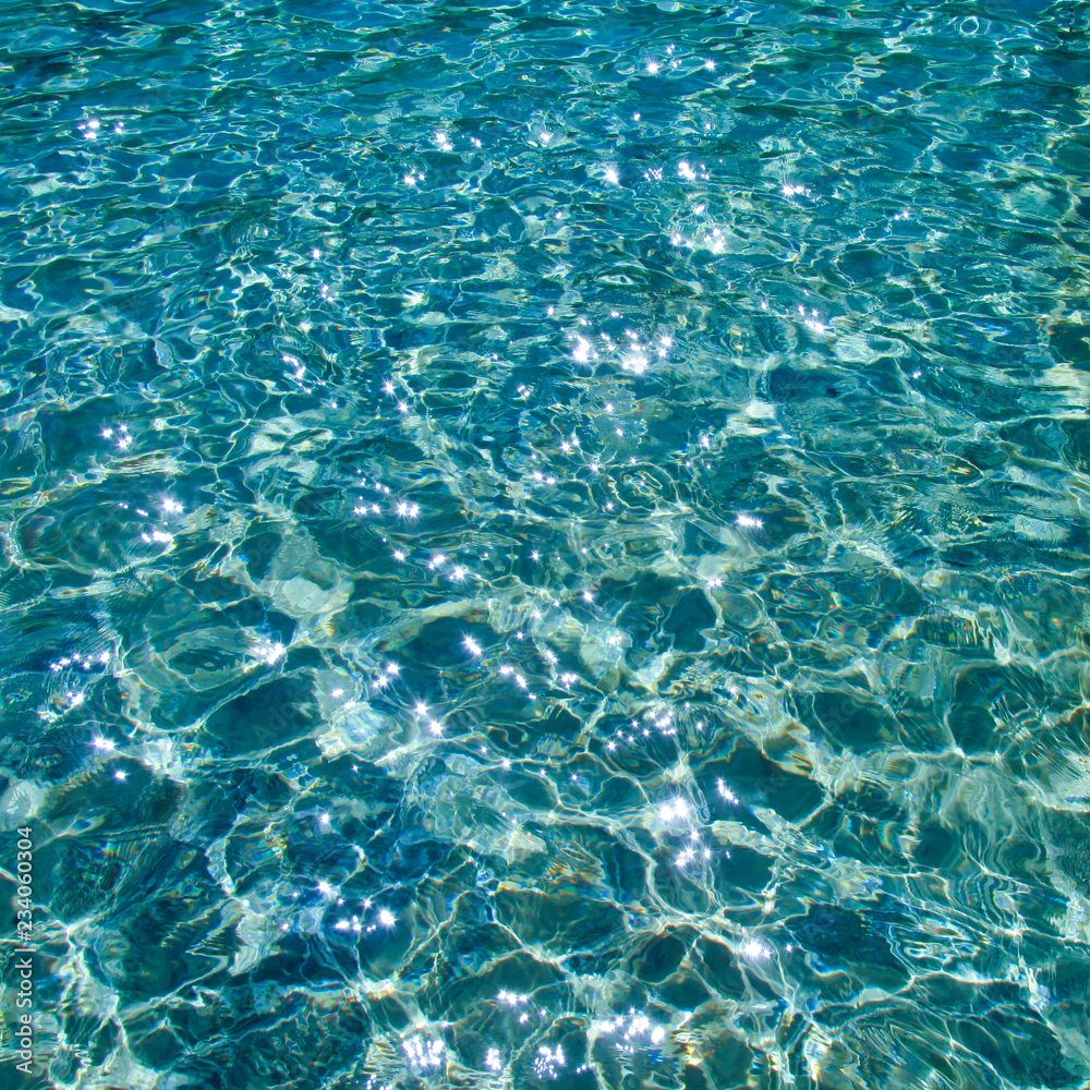 Blue transparent water surface with bright sun glare and sunny shining reflections on bottom. Top view of turquoise ripple texture with sunlight refracting through liquid layer.