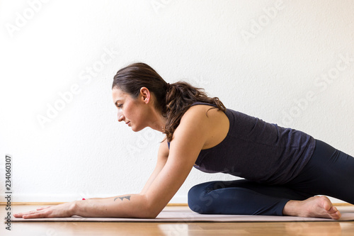 Close-up side view of a young woman working out at home, doing the Sleeping Swan yin yoga posture, medium length.