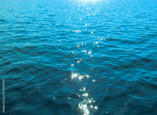 Bright blue rippled water surface and shine of sun glare on waves. Beautiful background image of abstract calm sea, lake, river, pond.