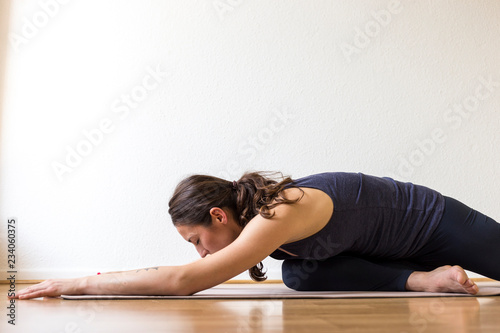 Close-up side view of a young woman working out at home, doing the Sleeping Swan yin yoga posture, medium length.