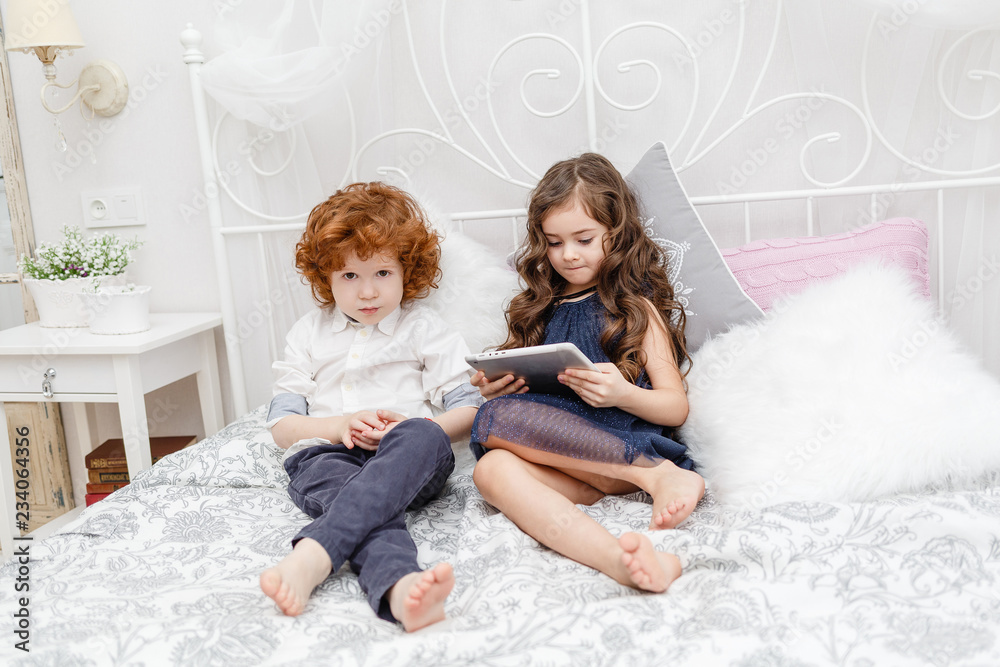 cute little girl with a boy sit on the bed and play in the tablet cute little girl with a boy sit on the bed and play in the tablet