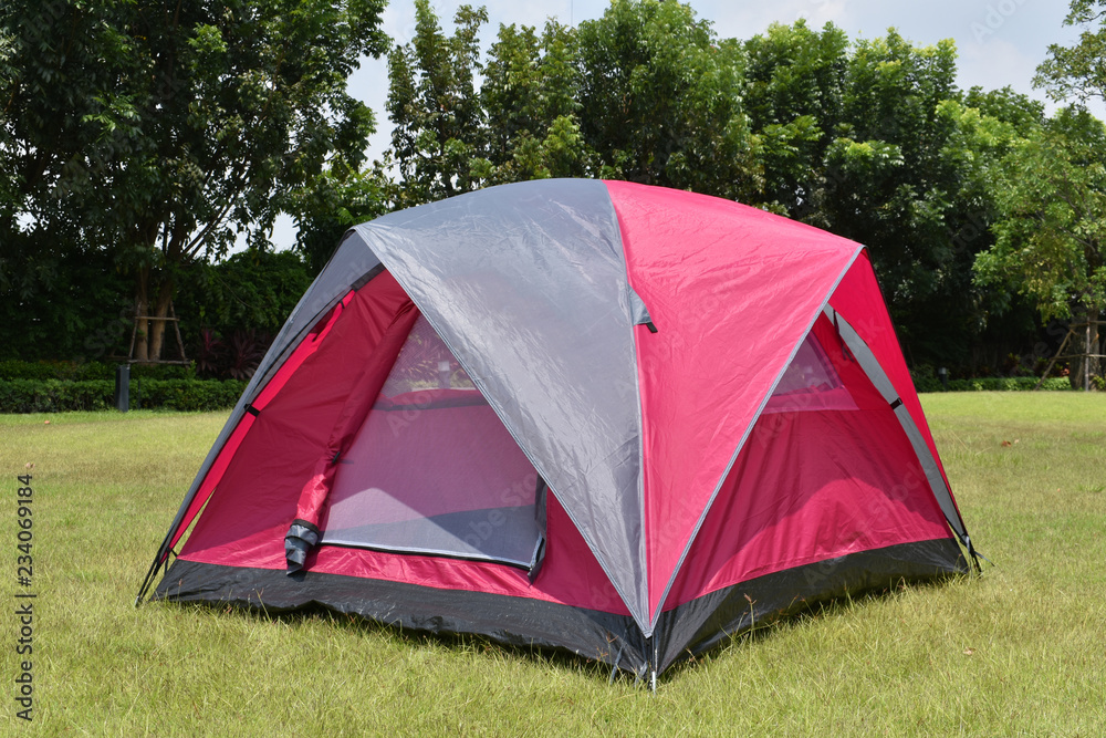 Pink color camping tent with rain fly expanded on green field.