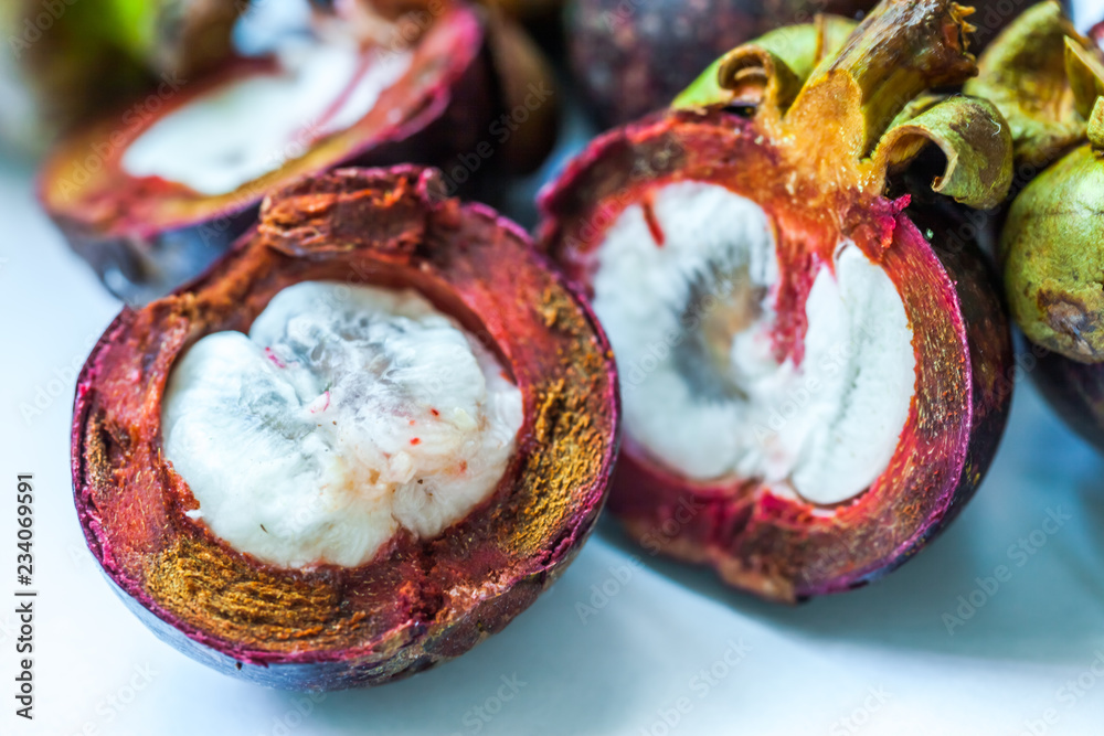 Naklejka premium Mangosteen fruit and cross section showing the thick purple skin and white flesh of the queen of fruits in China.