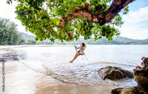 Beautiful young woman traveler swinging on a swing on a tropical island in the background of amazing landscape