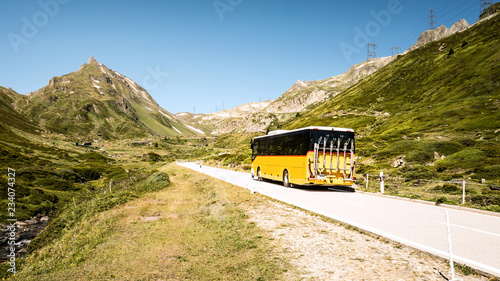 Public transportation in the mountains of switzerland named Postauto. Yellow bus on the road.
