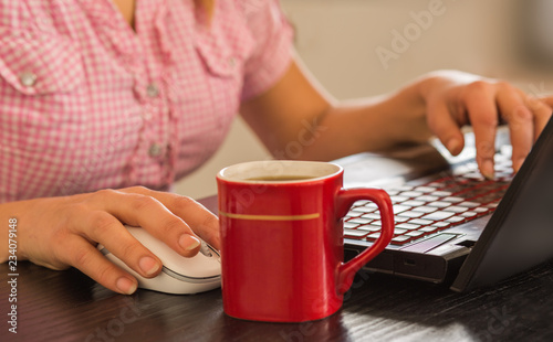Woman working on laptop with cup of coffee.