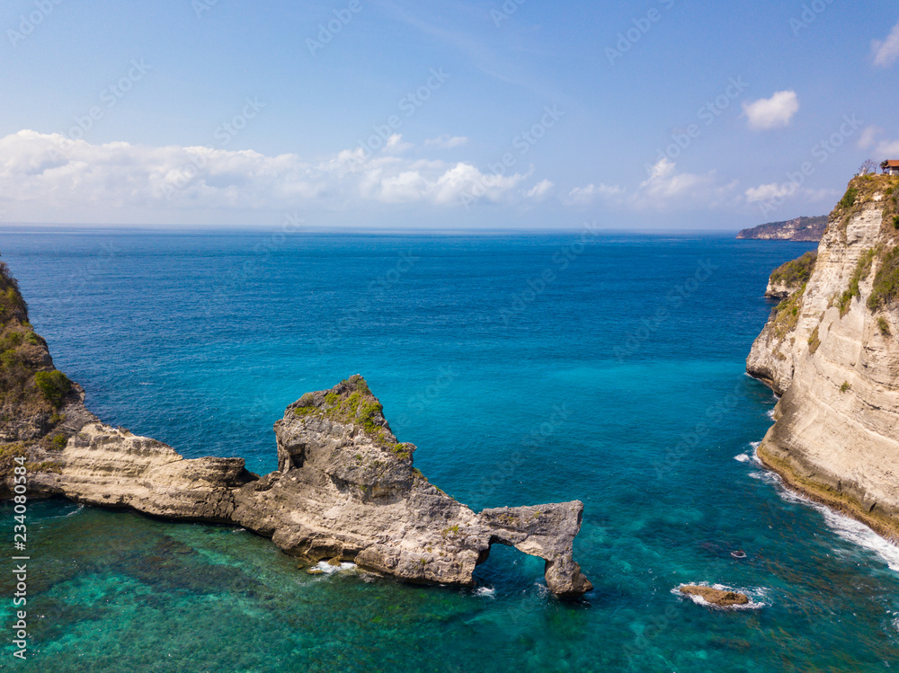 Naklejka premium Aerial view to beautiful arched rock in ocean on Atuh beach. Photo from drone. Nusa Penida, Bali, Indonesia
