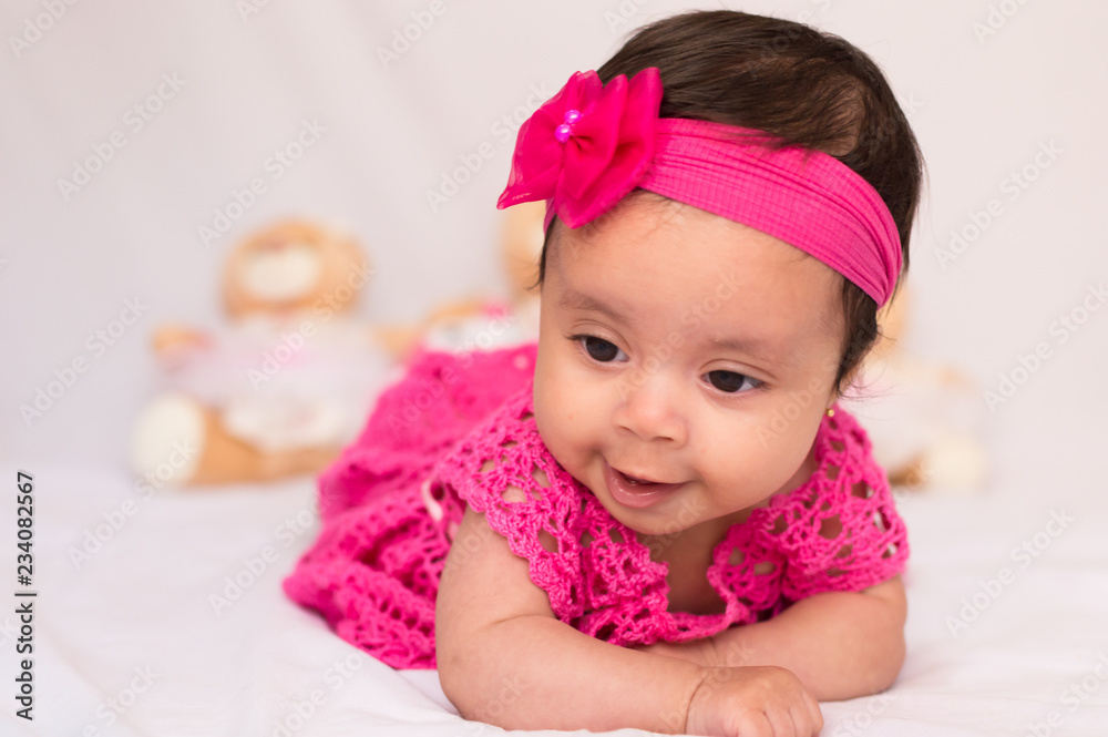Smiling baby in pink dress with teddy bear in blurred background Smiling baby in pink dress with teddy bear in blurred background