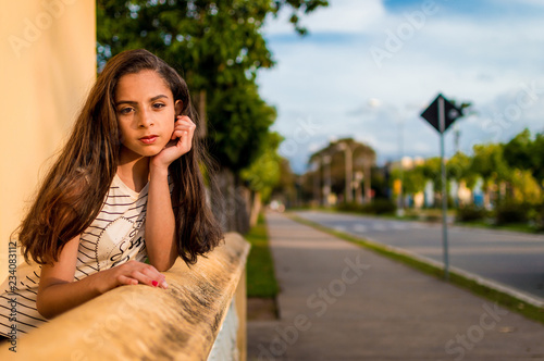 Photography Pretty brown-haired girl leaning against wall with blurred street in background
