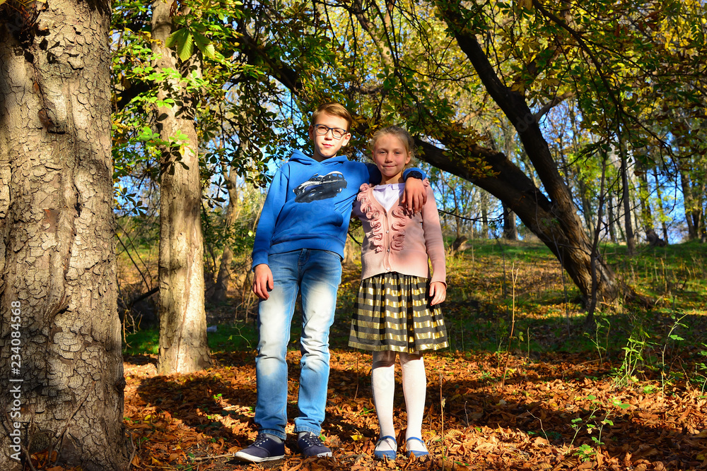Fototapeta premium A boy with a girl are embracing in the forest on dry leaves on a summer evening, brother and sister in nature.