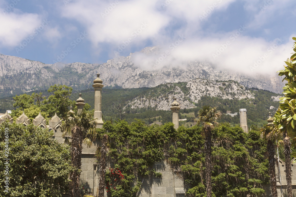 A wall with Moorish turrets, overgrown with lush greenery and a view of the peaks of AI-Petri in the clouds.Crimea.