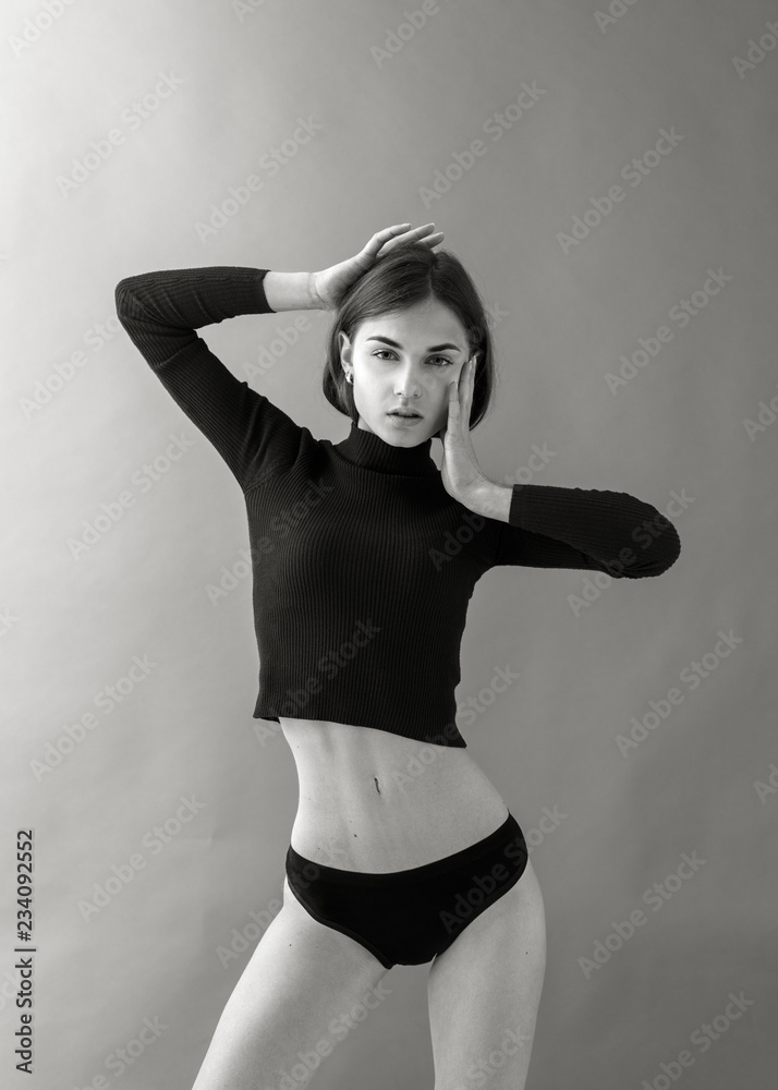 Foto de young beautiful woman posing in Studio stands in red sweater and  black lingerie.Standard model tests of young pretty woman on a gray  background,Test Shots young models for modeling agency do